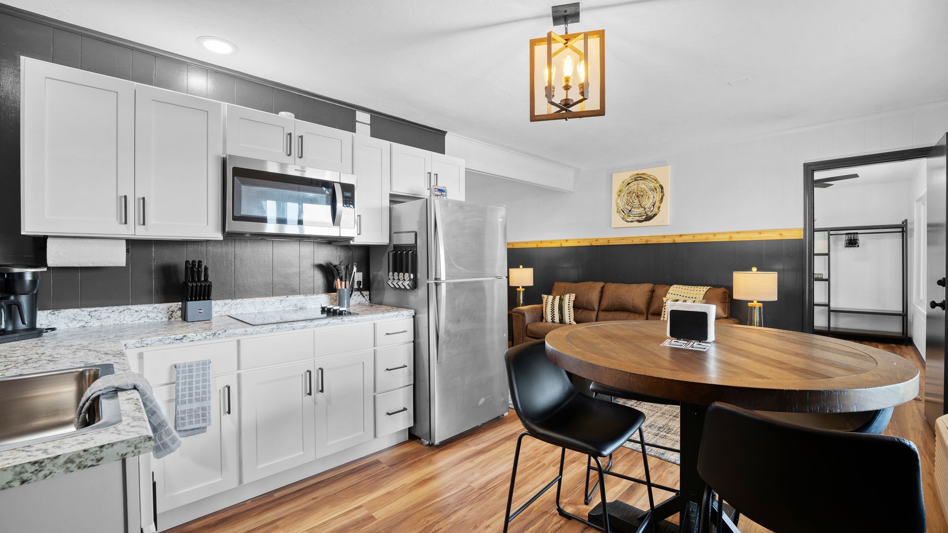 A bright kitchen and dining area with white cabinets, stainless appliances, a wooden table, and black chairs.