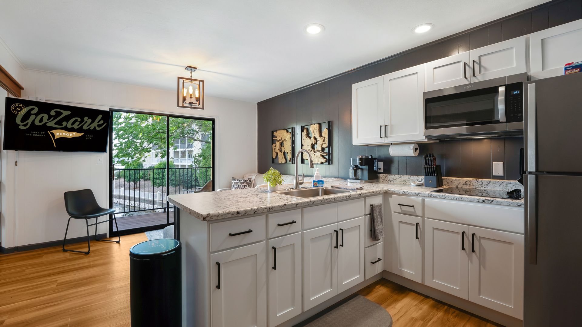 A bright modern kitchen with white cabinets, dark charcoal walls, and wood floors, featuring a breakfast bar and patio door.