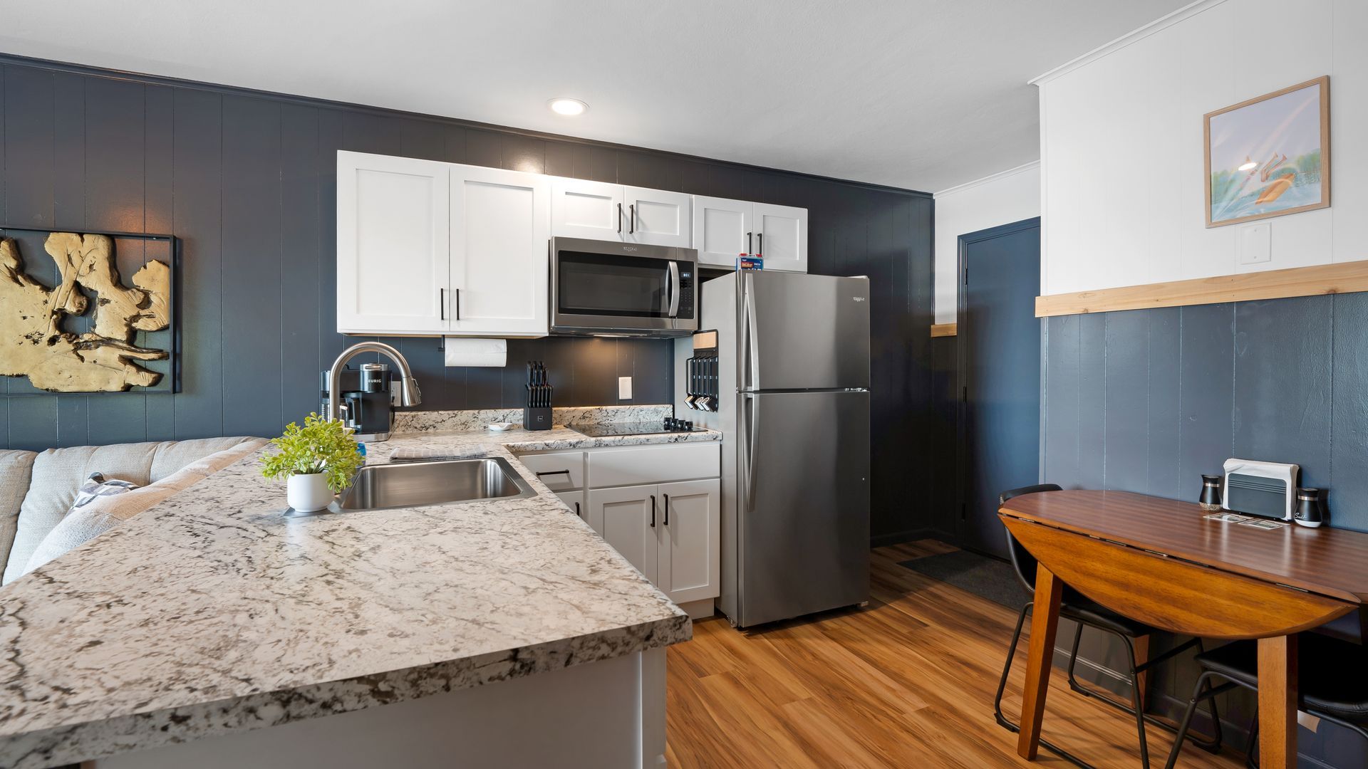 A modern kitchen with a granite island, white cabinets, dark blue walls, stainless appliances, and a wood dining table.