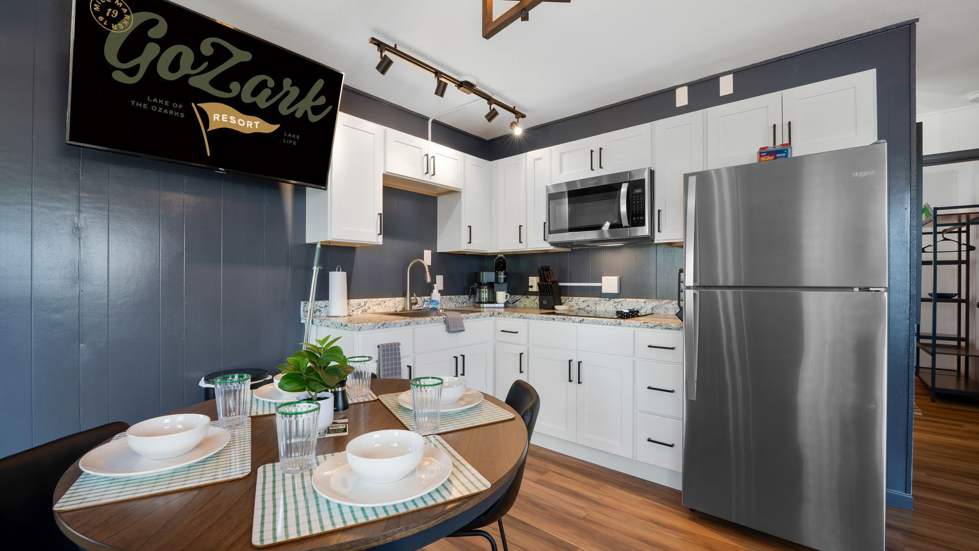 A small kitchenette with white cabinets, stainless steel appliances, and a round dining table with place settings.