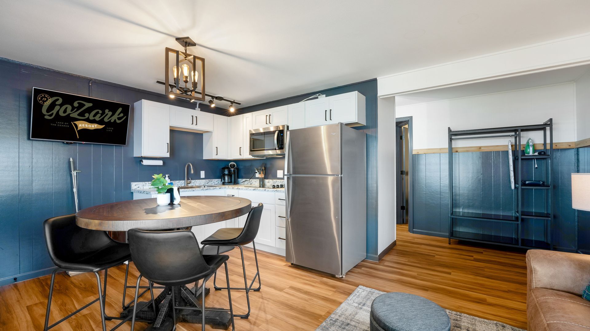 A modern kitchen with white cabinets, stainless appliances, a dark blue accent wall, and a circular wooden dining table.