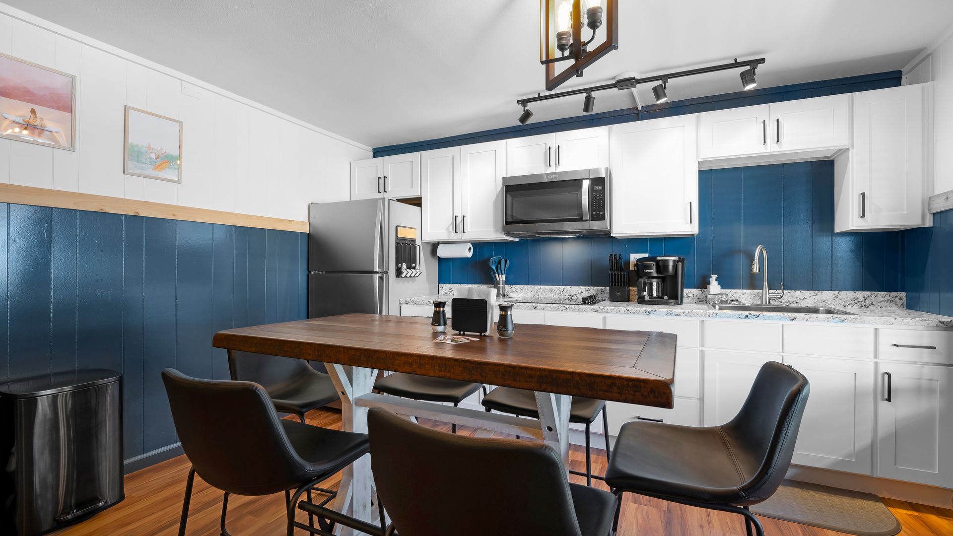 Kitchen with white cabinets, blue backsplash, and a wooden dining table with four black chairs on wood flooring.