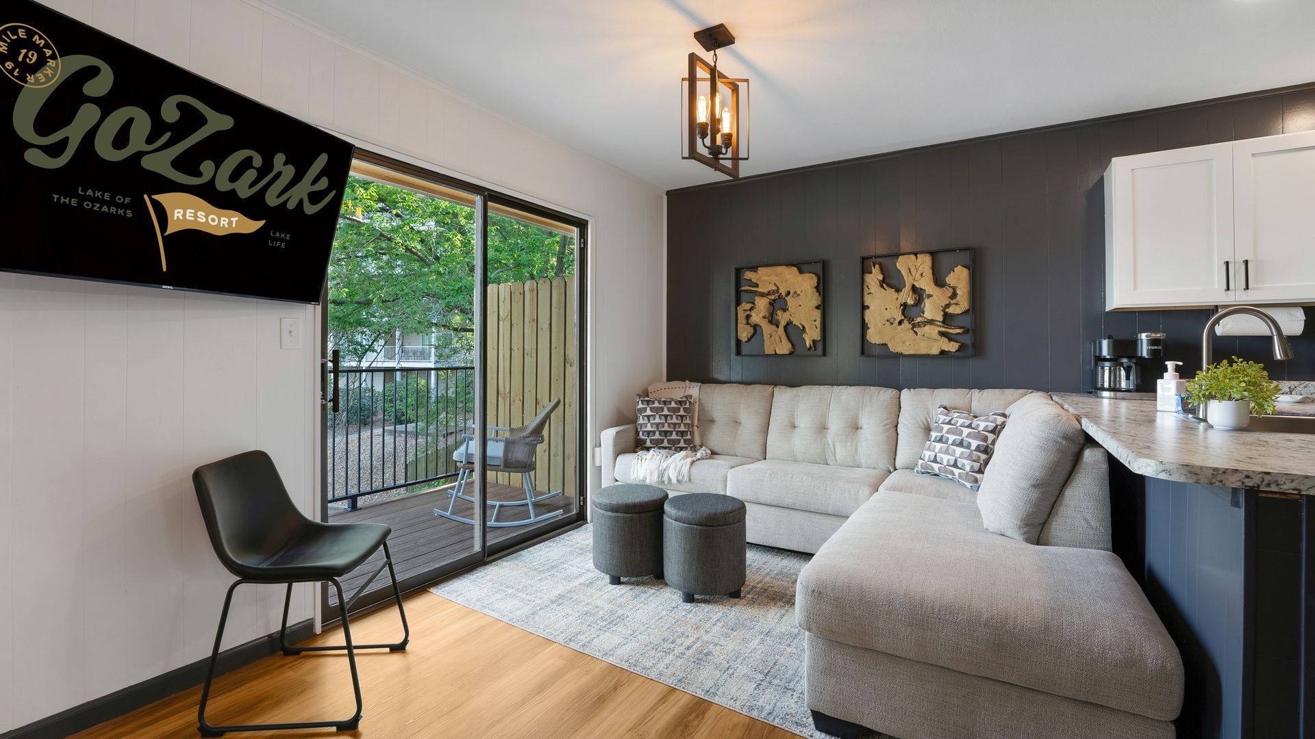 A modern apartment living room with a sectional sofa, two ottomans, a black chair, and a sliding door leading to a patio.