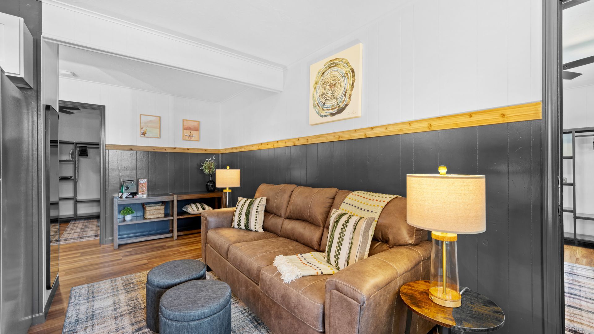 A brown leather couch with patterned pillows sits in a living room with dark gray paneled walls and a wooden trim.