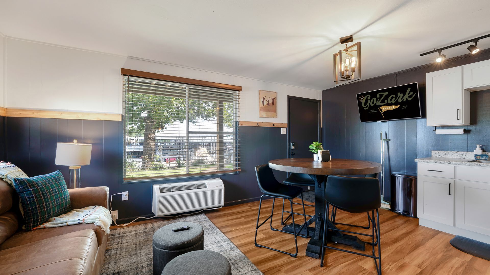 A modern, cozy room with a leather couch, a round dining table with black chairs, and white cabinets against dark walls.