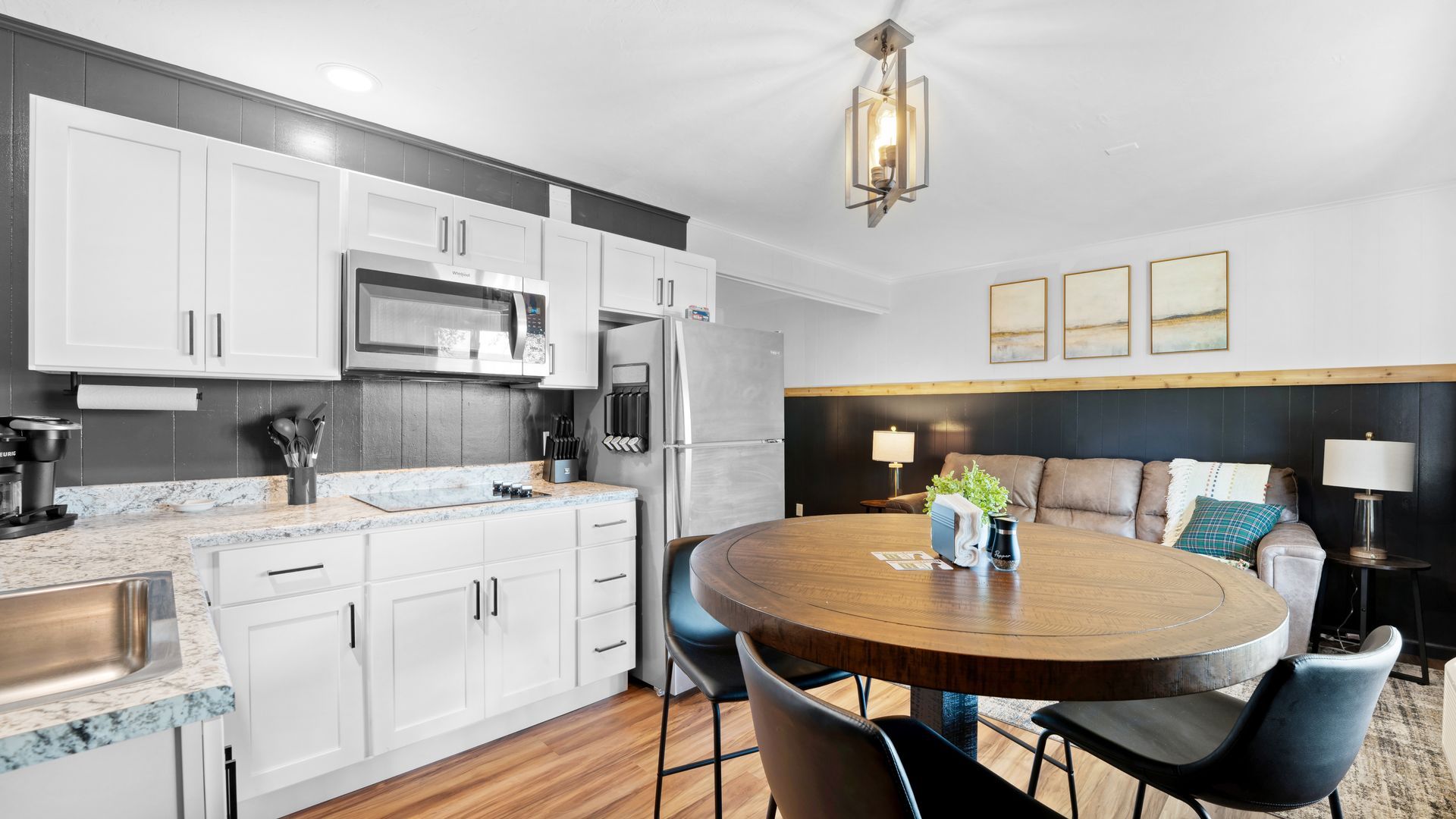 A modern kitchen featuring white cabinets, stainless steel appliances, and a round wooden dining table with black chairs.