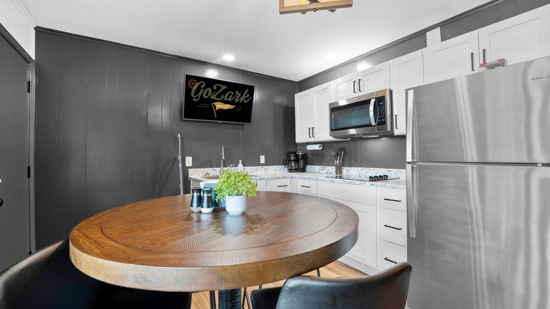 Modern kitchen with dark grey panel walls, a round wood dining table, white cabinets, and stainless steel appliances.