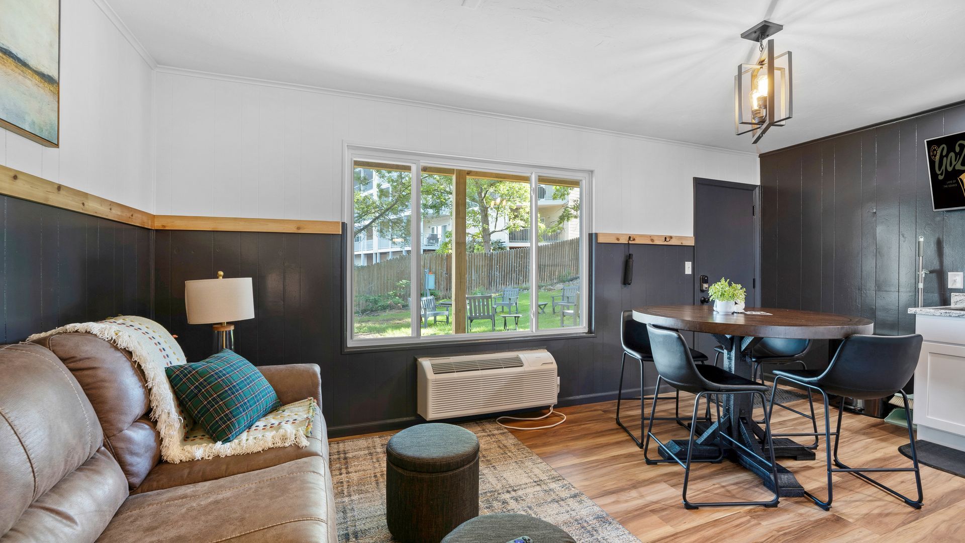 A living and dining area with a brown leather couch, round wooden table, black chairs, and dark paneling on the walls.