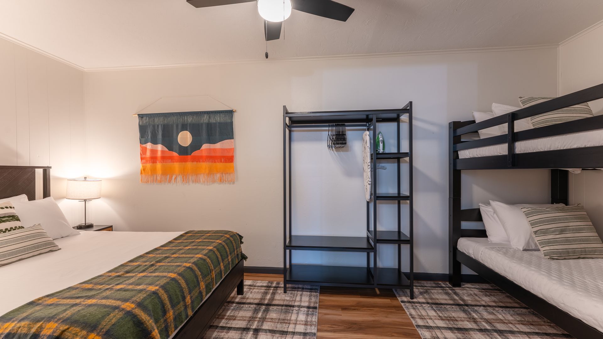 A bedroom featuring a large bed with a green plaid blanket, a black open wardrobe, and a black bunk bed on a plaid rug.