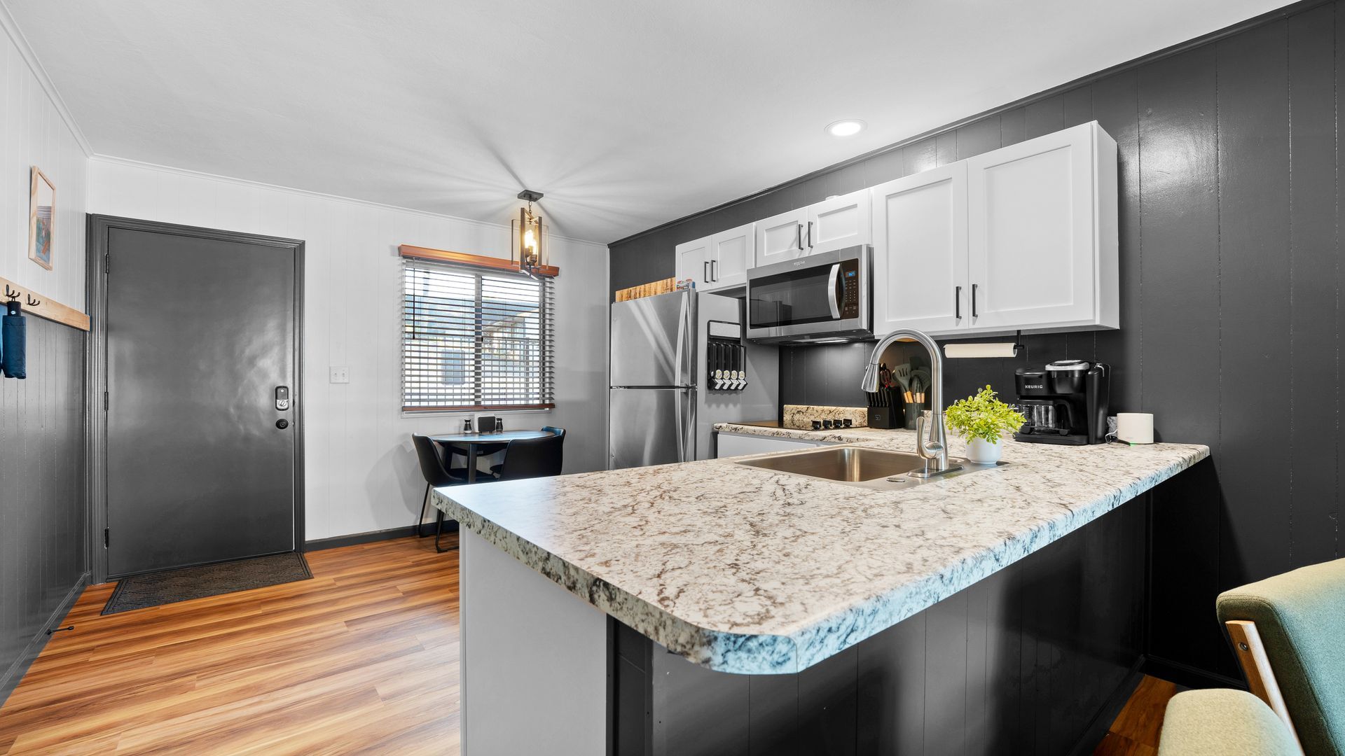 A kitchen with light stone countertops, white cabinets, stainless steel appliances, and dark walls near a dining area.