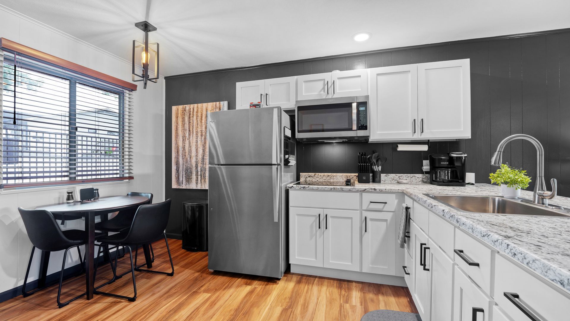 A small kitchen with white cabinets, a stainless steel refrigerator, granite countertops, and a dining table with chairs.