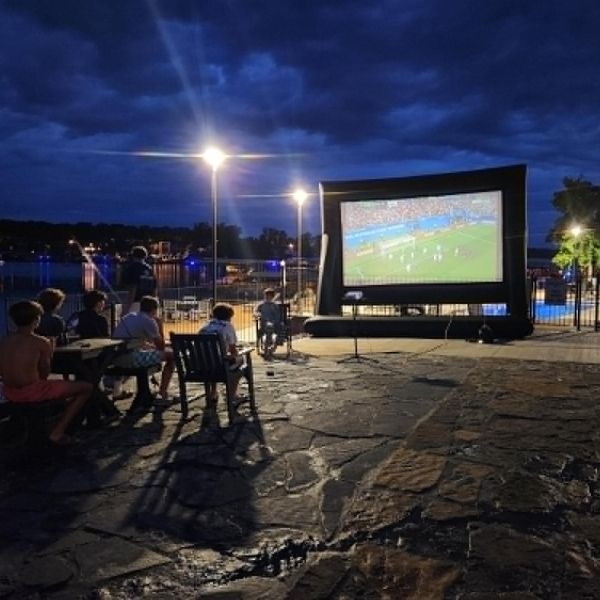People watching a soccer match on a large outdoor screen at night