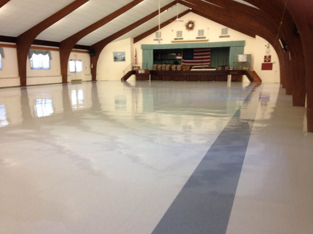 Large hall with a polished, light-colored floor; stage at the back with an American flag.