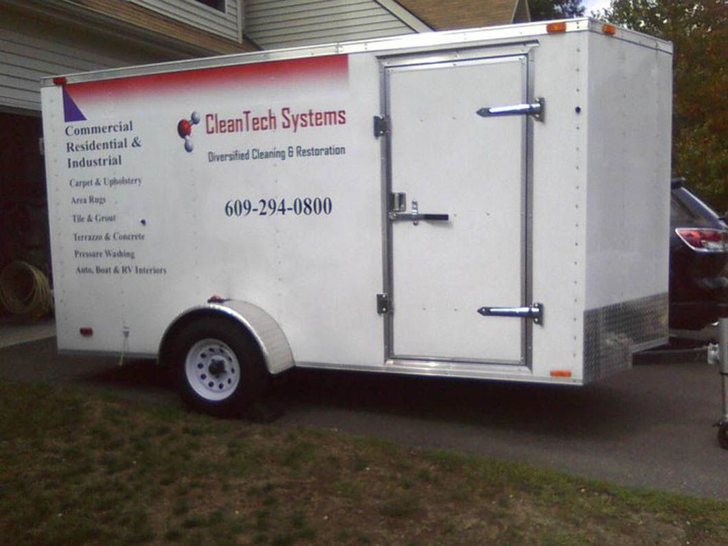 White trailer with business logo and phone number parked on driveway.