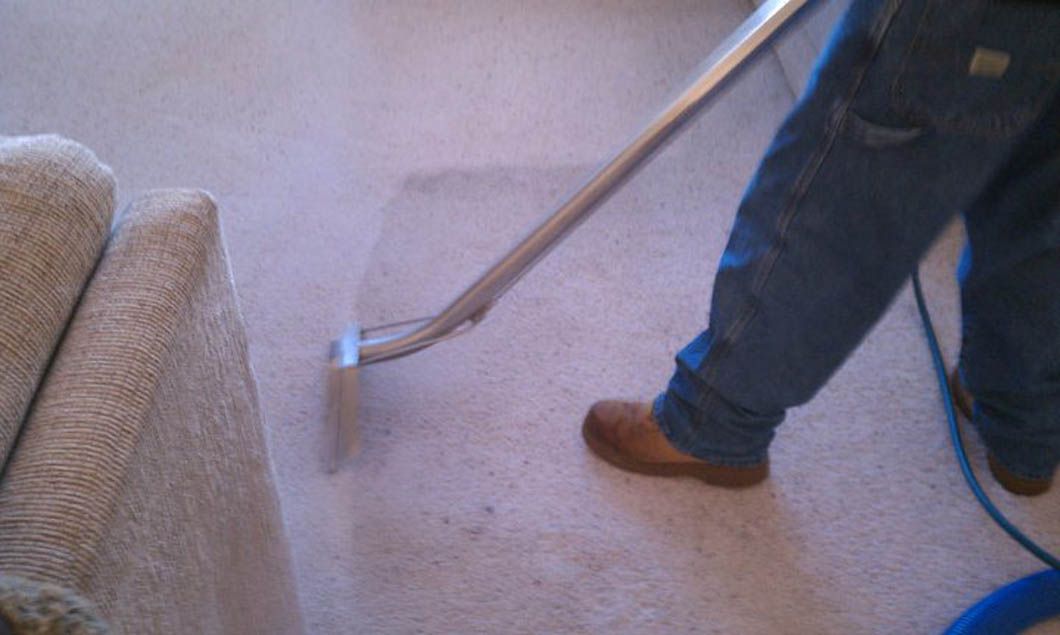 Person cleaning a carpet with a steam cleaner next to a beige couch.