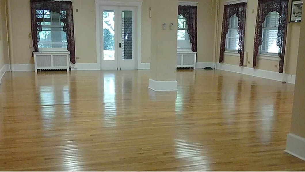 Empty room with shiny, light-colored wooden floors and windows with dark curtains.