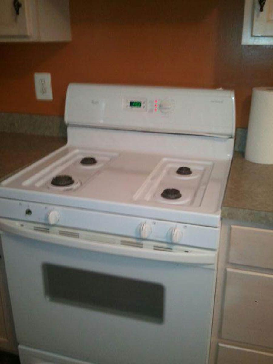 White gas range with four burners, oven, and digital display in a kitchen.