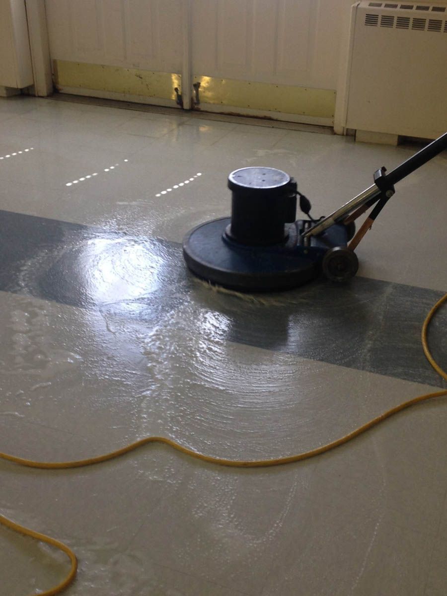 Floor polisher cleaning a gray and white floor; yellow cord present.