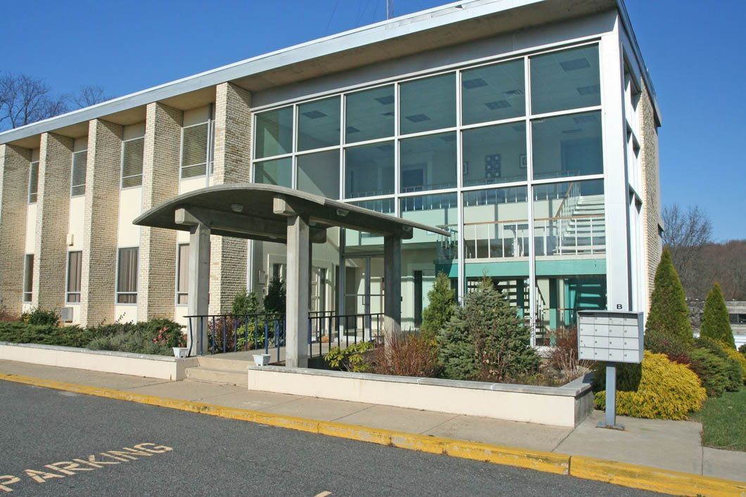 Two-story modern building with large glass windows and a small covered entrance. Sunny day, exterior shot.