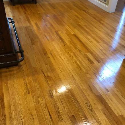 Shiny, light-brown hardwood floor with wood grain. Reflection of light on the glossy surface.