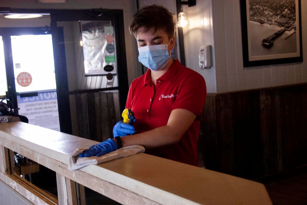 Person in red shirt and face mask sanitizing a counter in a restaurant.