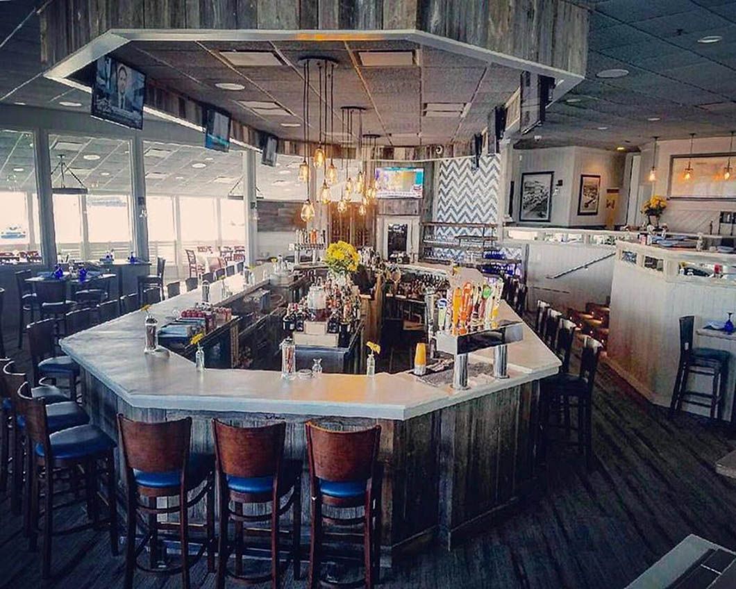 Bar interior with wooden accents, marble counter, and blue bar stools; windows in the background.