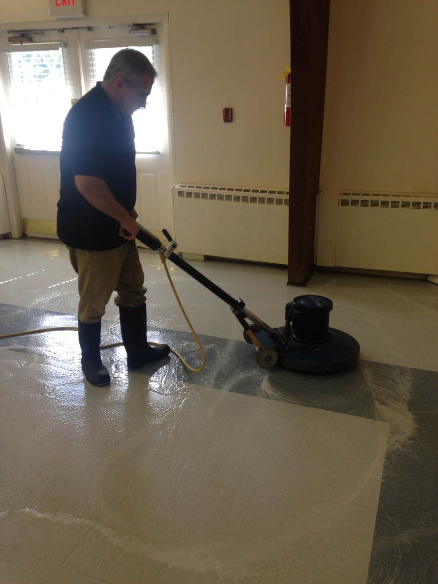 Man using floor buffer to clean a large, light-colored floor, wearing boots.