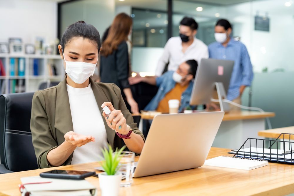 Woman in the office - wearing a mask and spraying alcohol