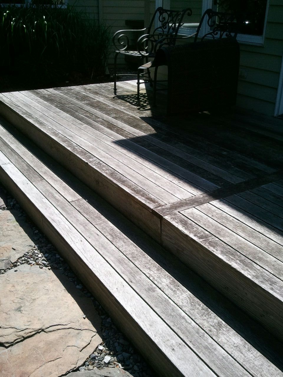 Wooden deck steps leading to a deck with furniture. The wood is weathered and gray.
