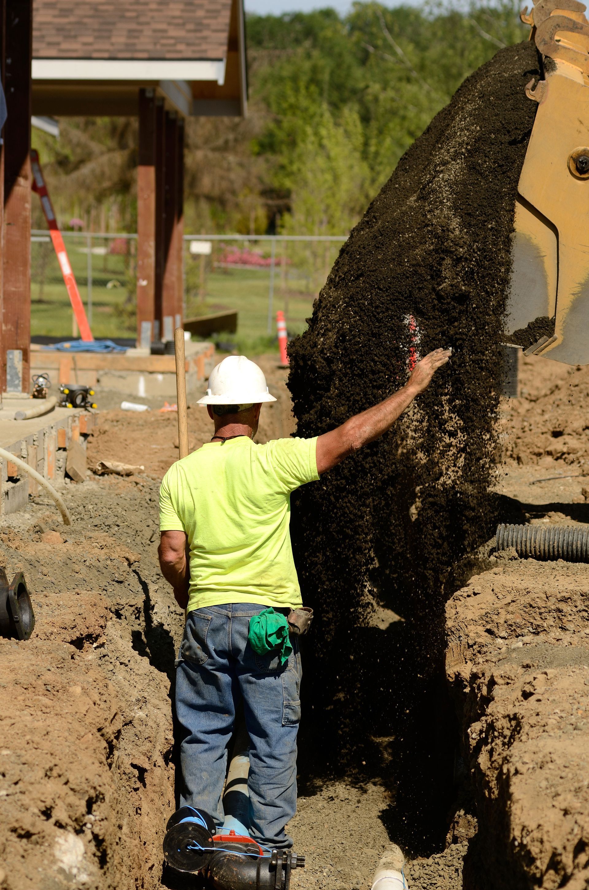 Worker in white hard hat touching a large dirt wall at a construction site