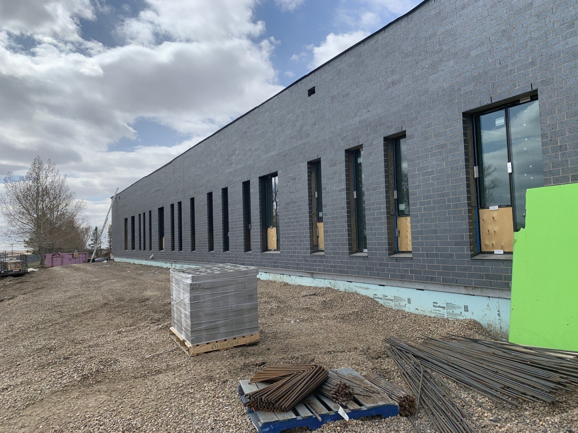 Gray brick commercial building under construction with tall windows and building materials scattered outside