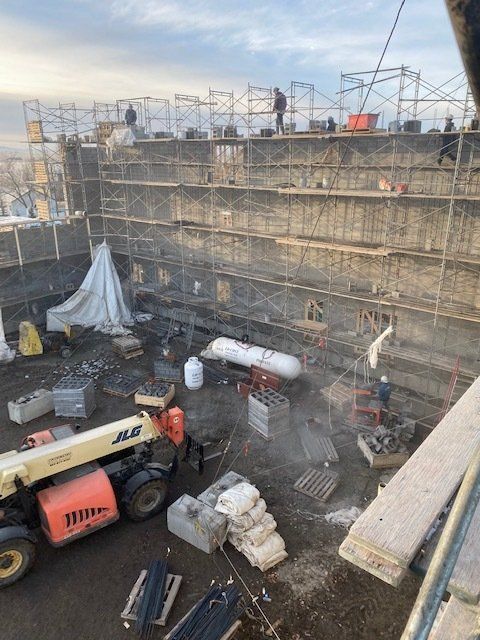 Construction site with scaffolding, heavy equipment, and workers on a concrete building facade