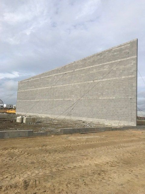Large slanted concrete retaining wall beside a dirt lot under a cloudy sky