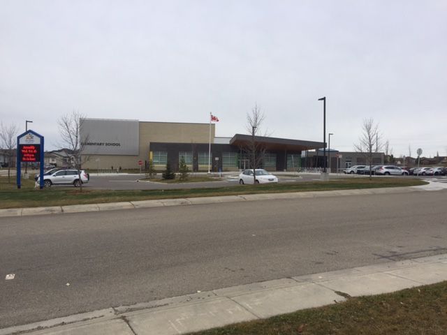 A roadside strip mall with shops, parked cars, and a large sign on a cloudy day.