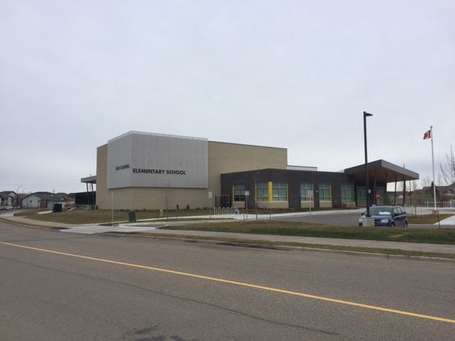 Small modern civic building with flagpoles and a parking lot on an overcast day