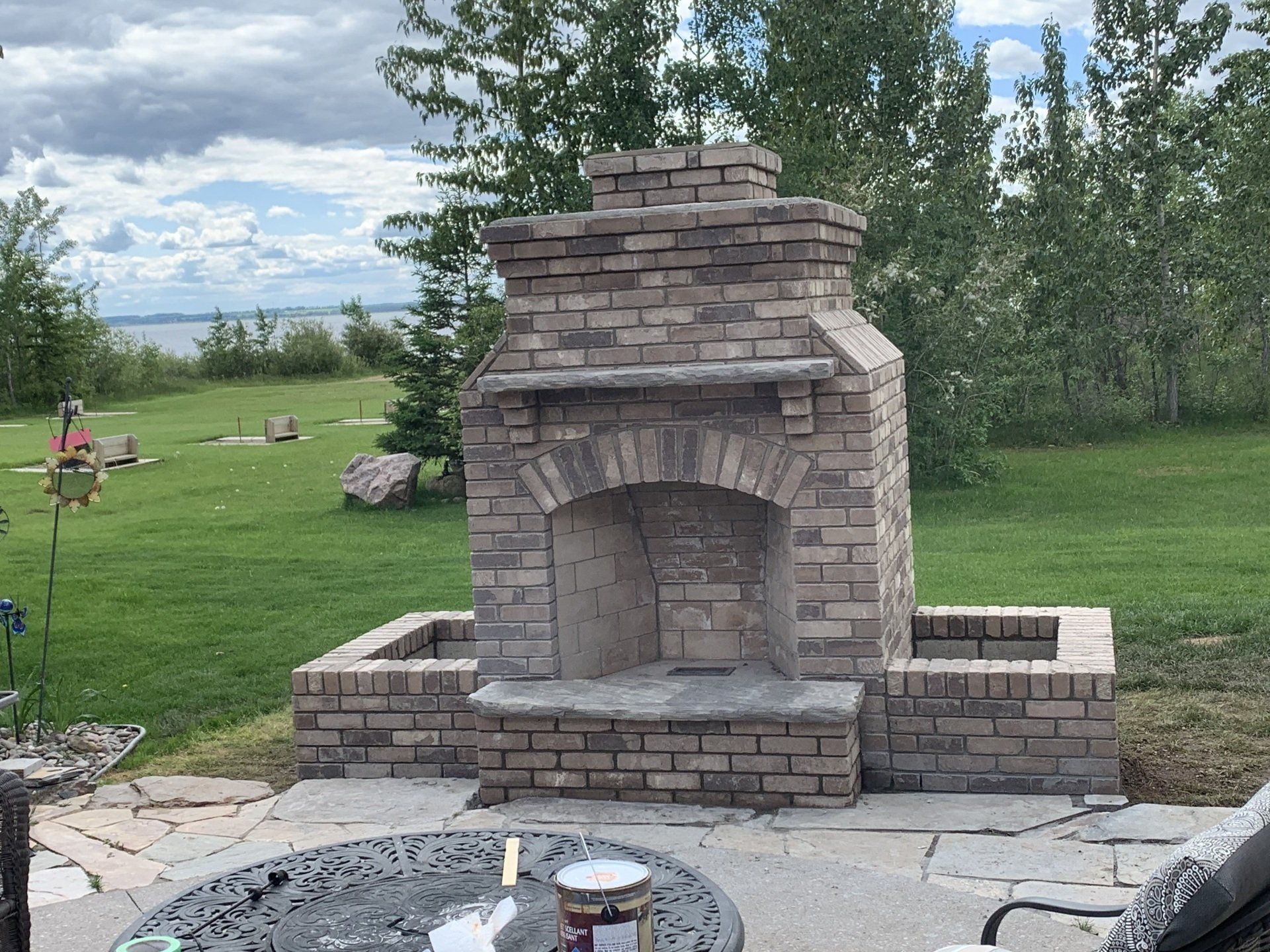 Stone outdoor fireplace with arched opening on a patio, set in a grassy backyard.