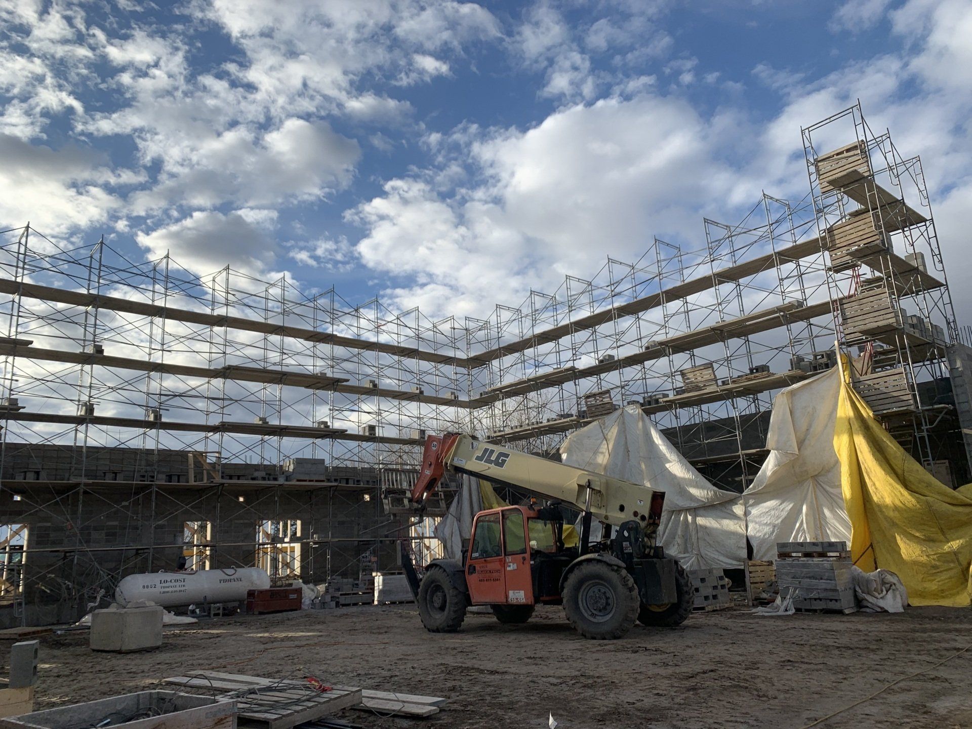 Construction site with scaffolding and cranes around a building frame under a cloudy sky