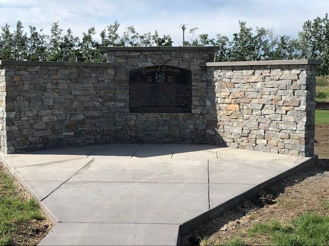 Stone outdoor fireplace set into a curved retaining wall beside a concrete patio.