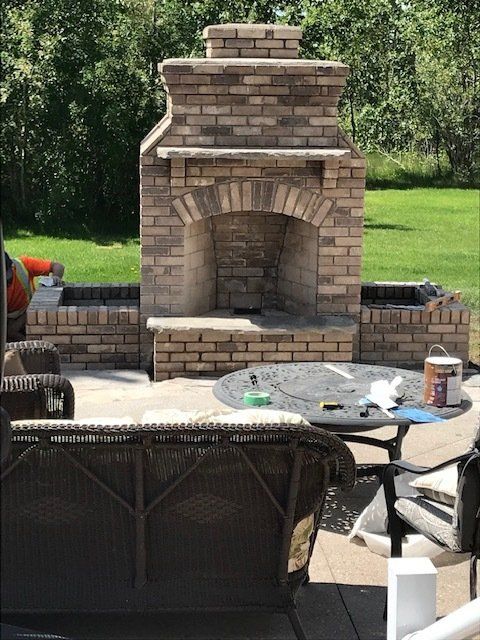 Outdoor brick fireplace with arched opening and chimney in a backyard patio, with chairs and a table in front