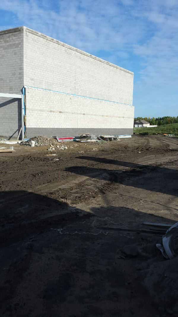White building with blue trim beside a muddy construction lot under a clear sky