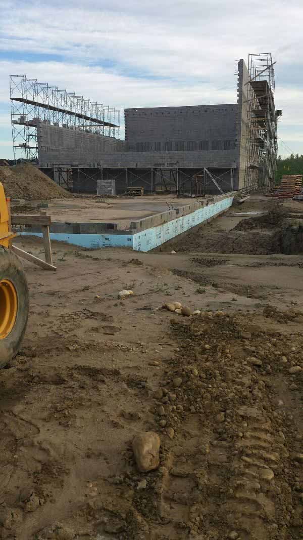 Muddy construction site with a large industrial structure and scaffolding in the background
