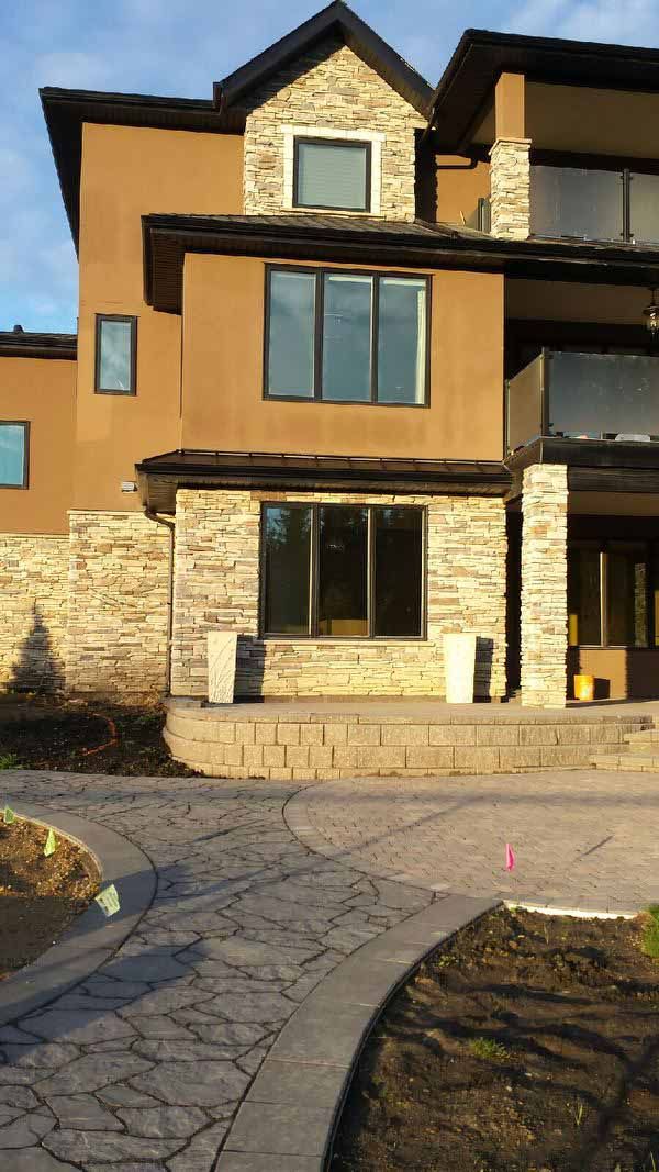 Modern two-story tan house with stone accents and a paved driveway in front
