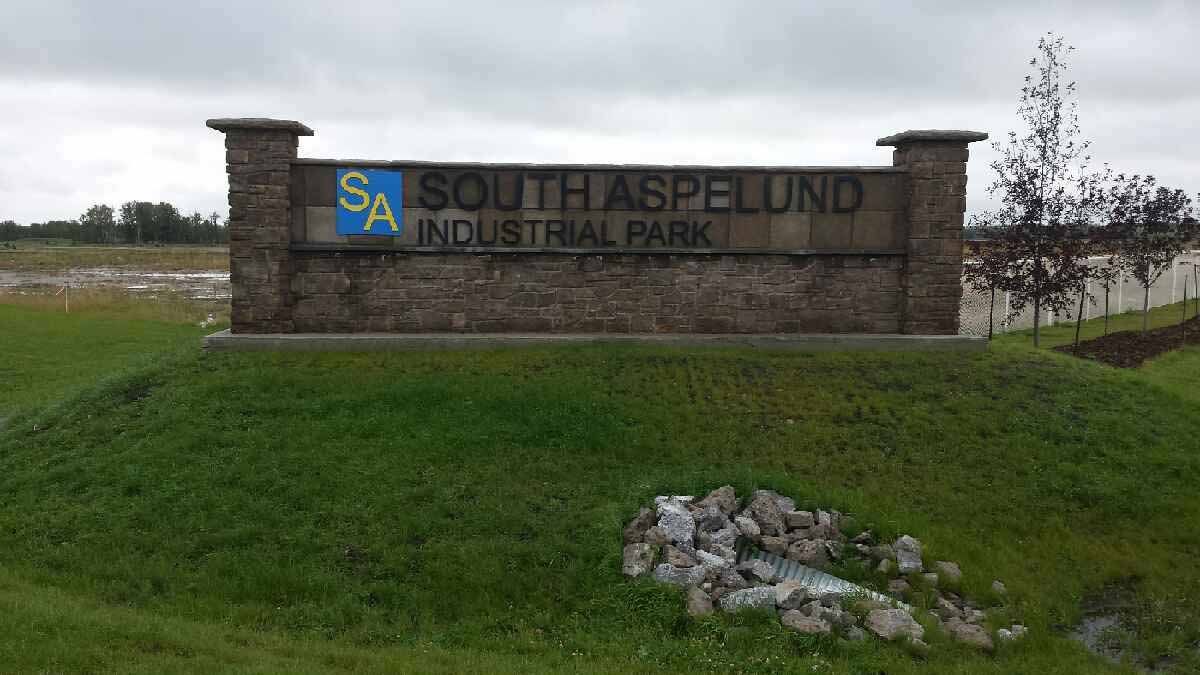 South Aspen Industrial Park sign on a stone wall beside a grassy roadside field.