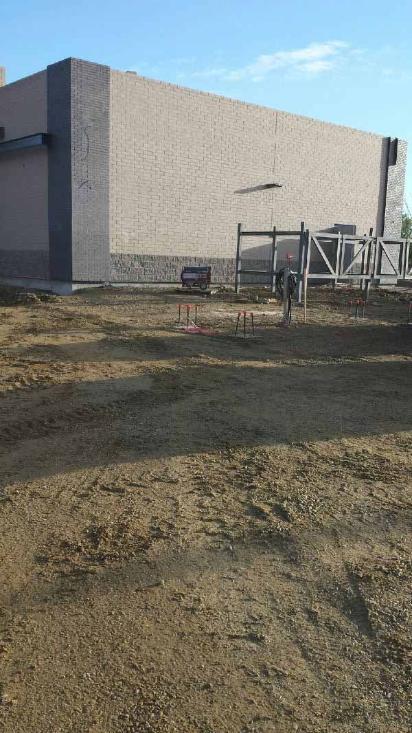 Large unfinished concrete building beside a muddy dirt lot with a small metal frame structure.