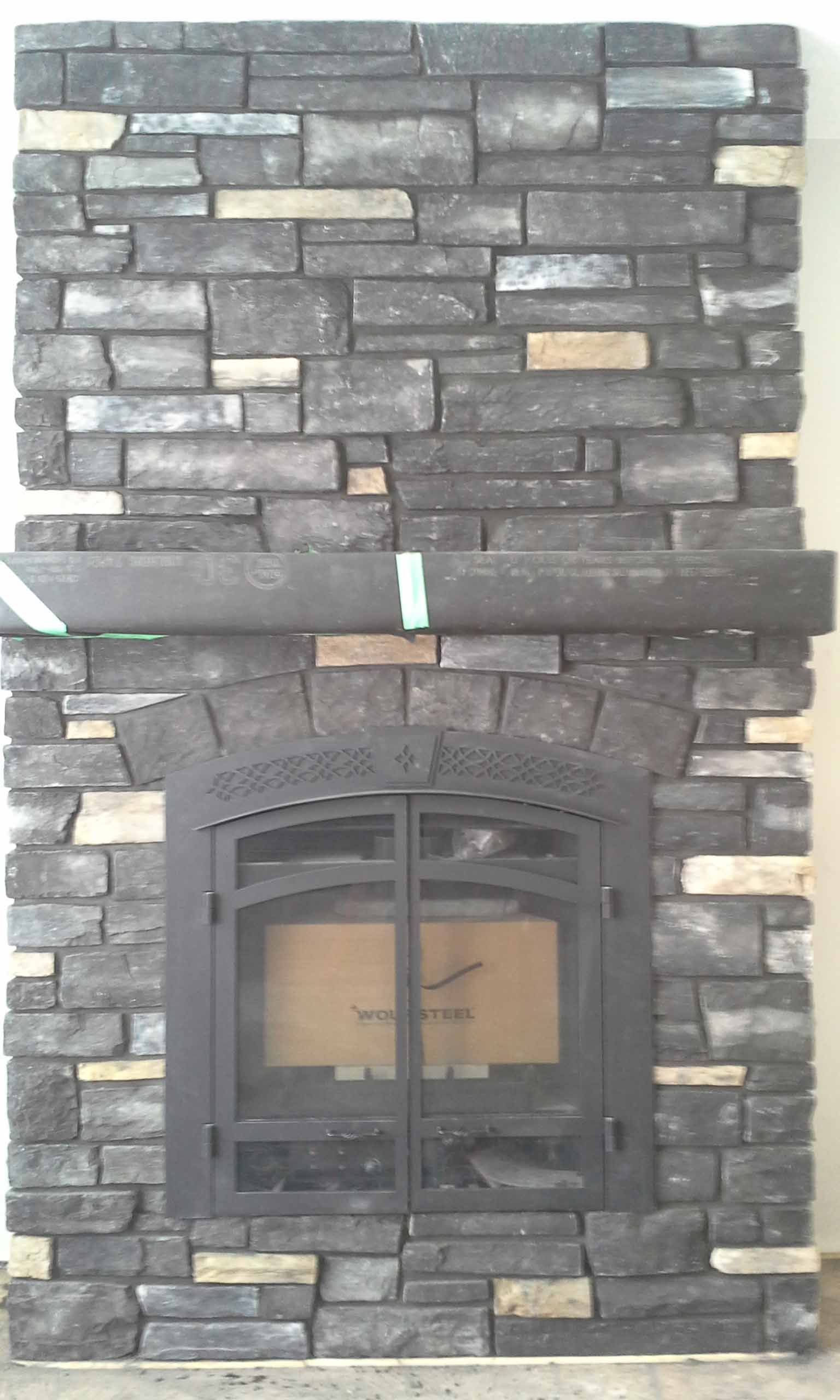 Stone fireplace wall with a black arched glass fireplace insert and stacked gray-brown stone veneer.