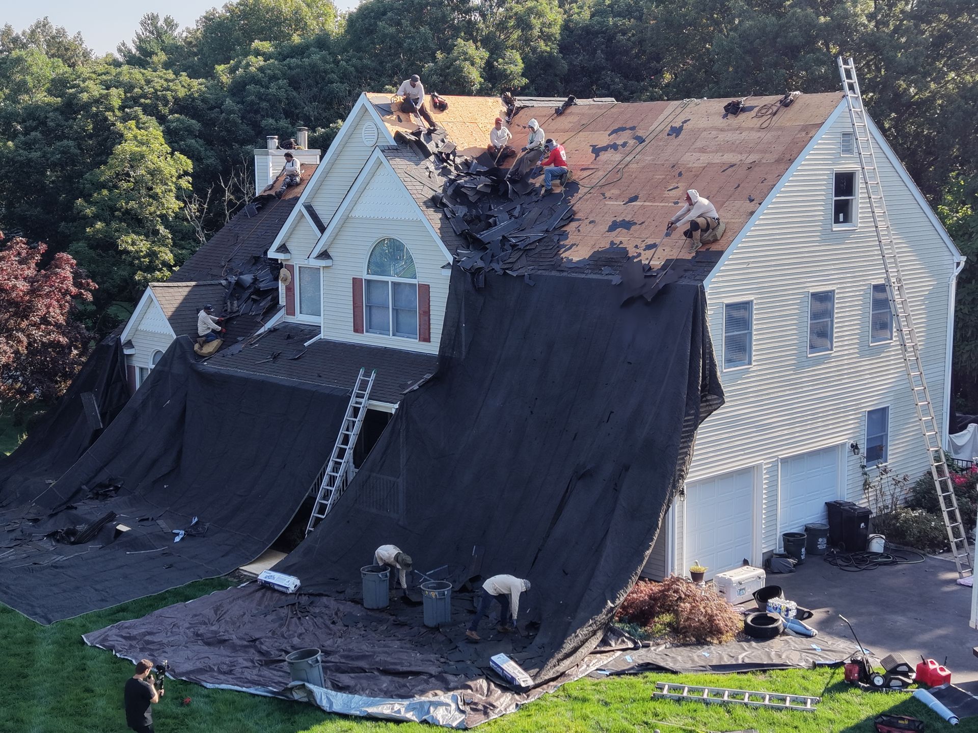 Aerial view of a house backyard with a wooden deck, patio furniture, and bare trees nearby.