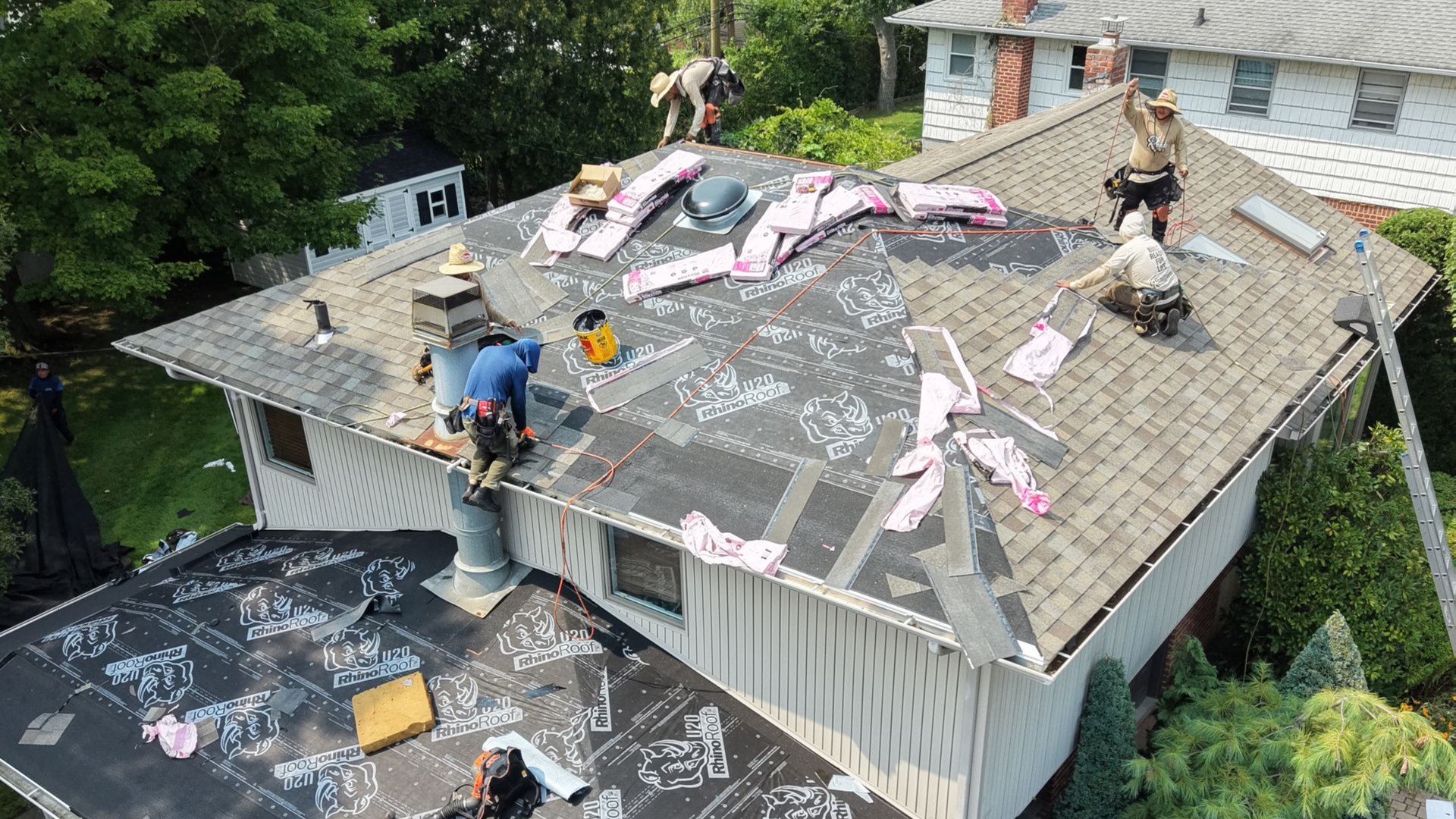 Workers repairing a damaged roof, with shingles torn off and debris scattered across the house.
