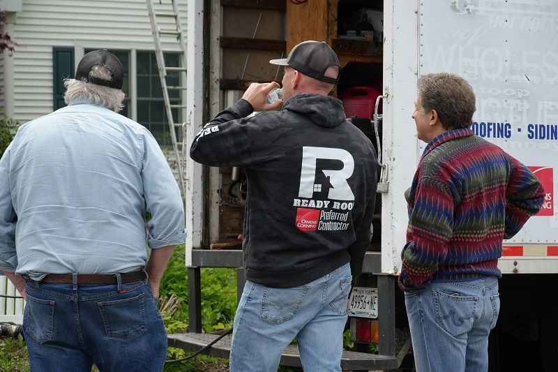 Three workers at a truck loading a cabinet, with one man carrying it through the open rear door.