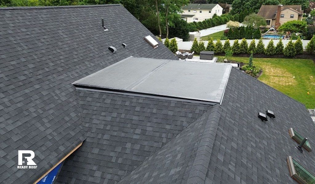 Gray roof with a large flat-roof addition and nearby houses in the background