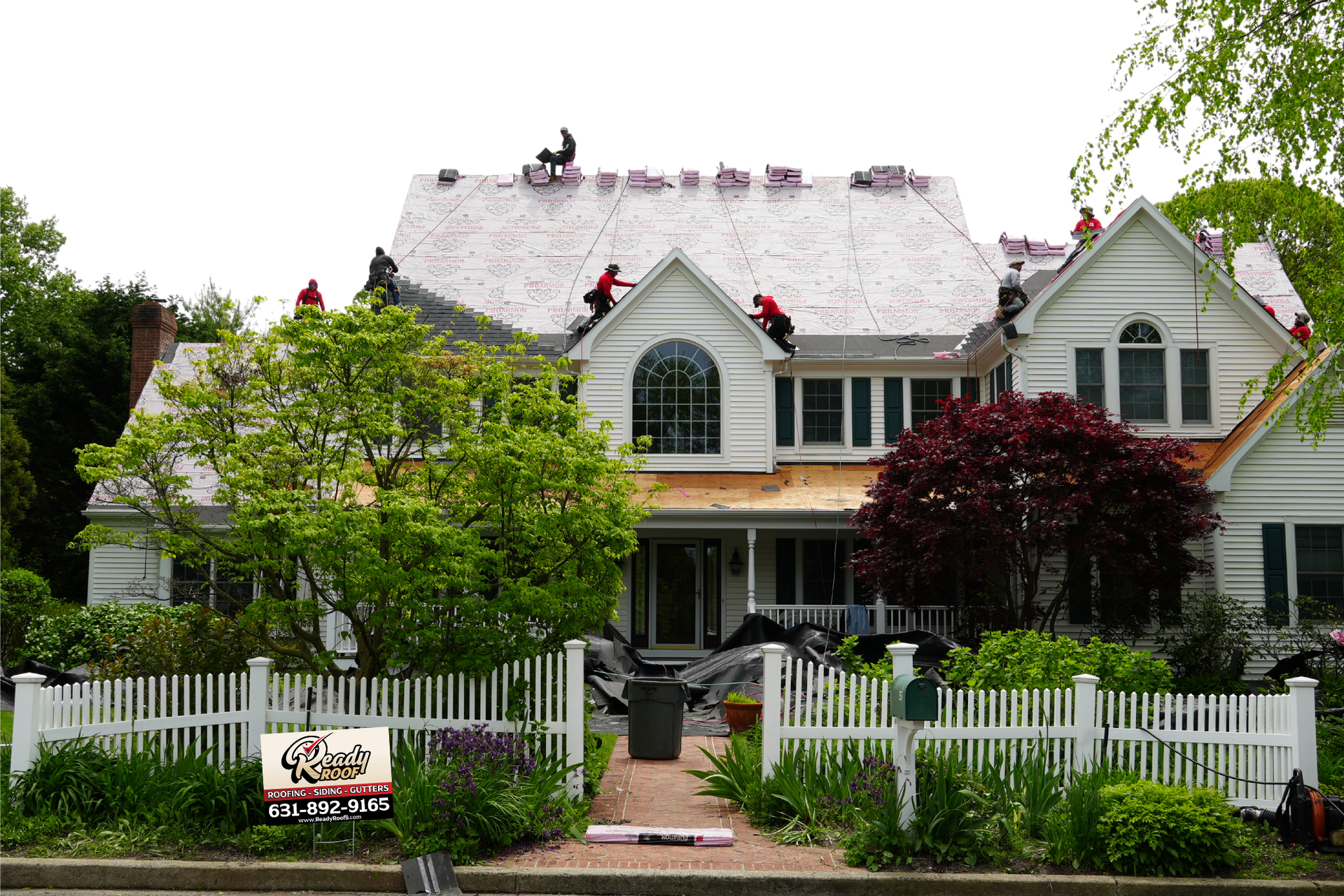 White house with steep roof, white picket fence, and lush front garden under overcast sky